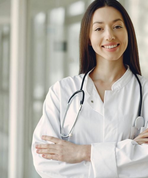Portrait of a smiling female doctor with arms crossed and stethoscope in a hospital corridor.